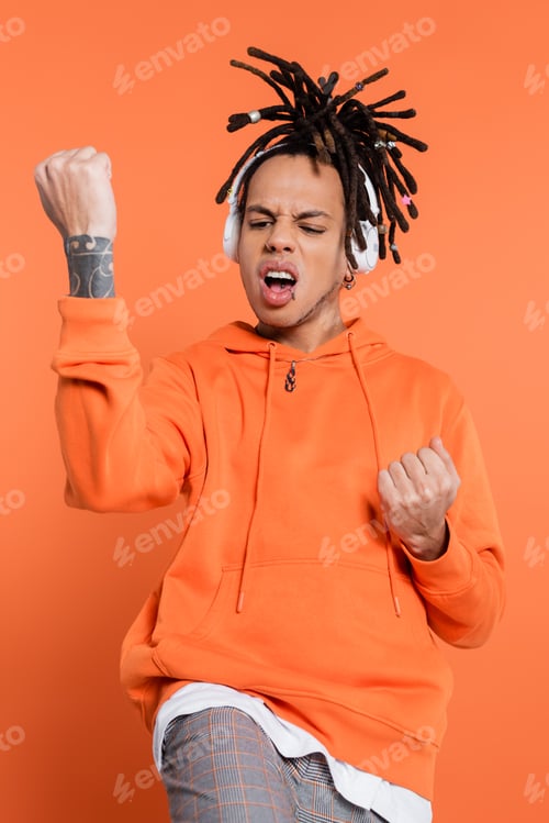 Preview: tattooed and emotional multiracial man listening music in wireless headphones and gesturing on