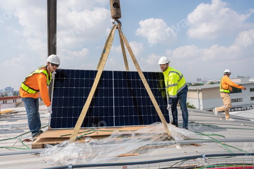 Preview: Men technicians carrying photovoltaic solar moduls on roof of factory.