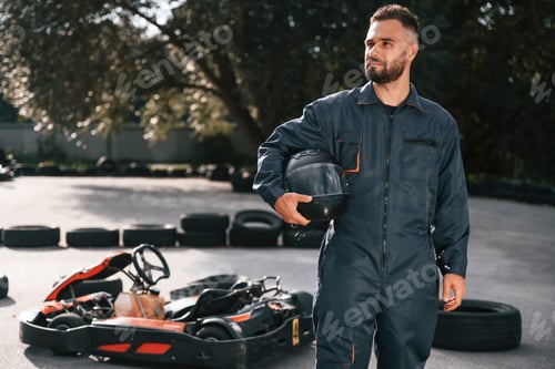Preview: Man Holding Helmet Stands Beside a Go-Kart