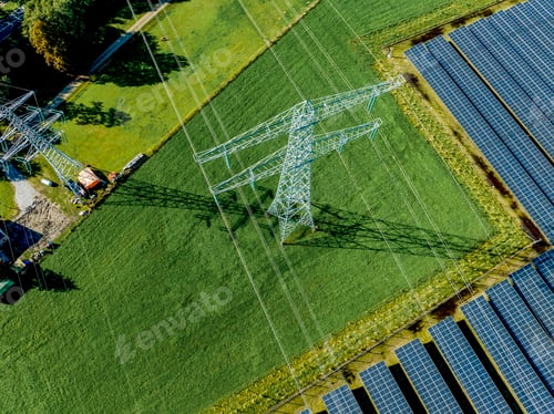 Preview: Aerial view of solar panels beside an electricity pylon on lush green fields