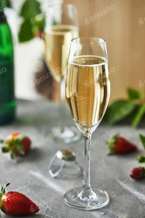 Preview: Glasses with champagne and strawberries on a gray background, with green leaves in the background