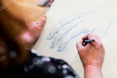 Preview: High angle close up of artist drawing human hand.