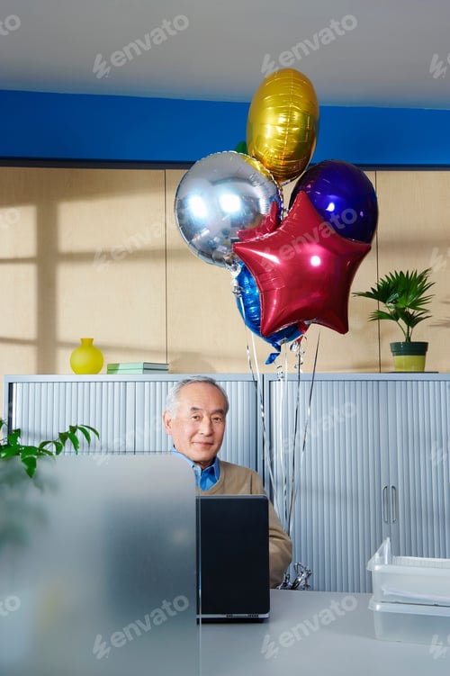 Preview: Senior man with balloons at office desk