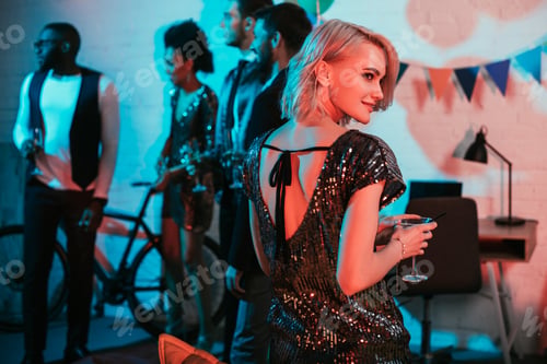Preview: Blonde woman holding glass with cocktail by friends at party