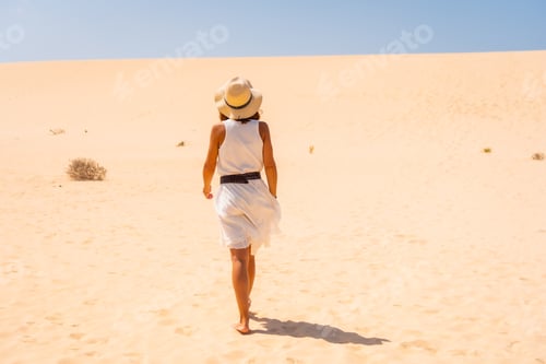 Preview: Tourist in white dress and hat walking through the dunes of the Corralejo