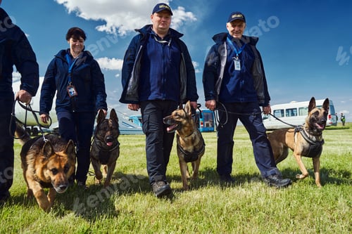 Preview: Cheerful security officers with detection dogs walking down airfield