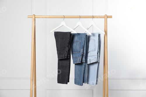 Preview: Many stylish jeans hanging from rack near white wall