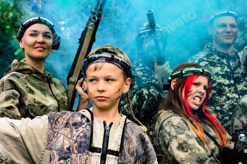 Preview: Cute boy in camouflage with friends celebrating winning laser tag shooting game with colored smoke N