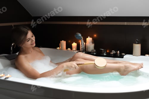 Preview: Beautiful woman rubbing leg with brush while taking bubble bath. Romantic atmosphere