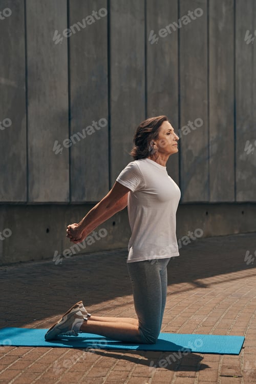 Preview: Relaxed senior slim female stretching arms outdoors