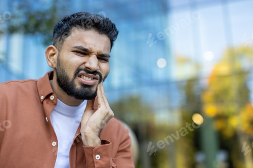 Preview: An Indian man suffering from a toothache, holding his cheek in pain.
