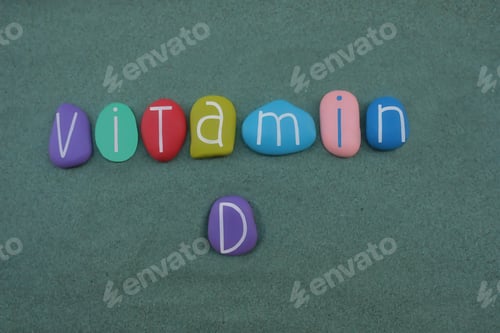 Preview: Vitamin D text composed with multi colored stone letters over green sand