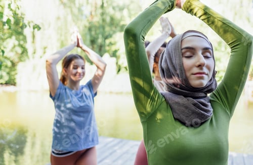 Preview: Group of teenages is engaged in fitness on pier by the lake or river.