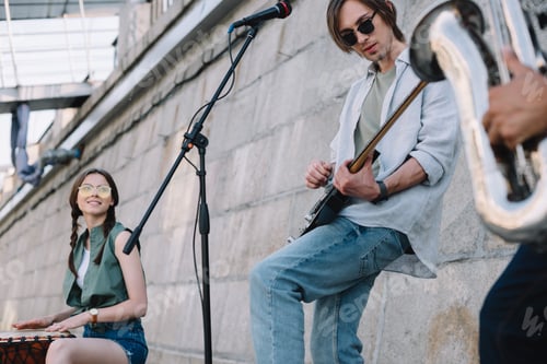 Preview: Young happy buskers with guitar, drum and saxophone at city street