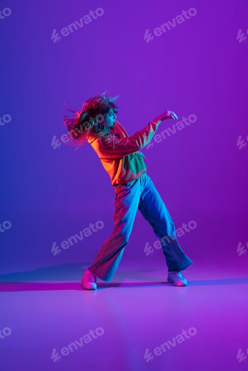 Preview: Stylish sportive girl dancing hip-hop in stylish clothes on colorful background at dance hall in