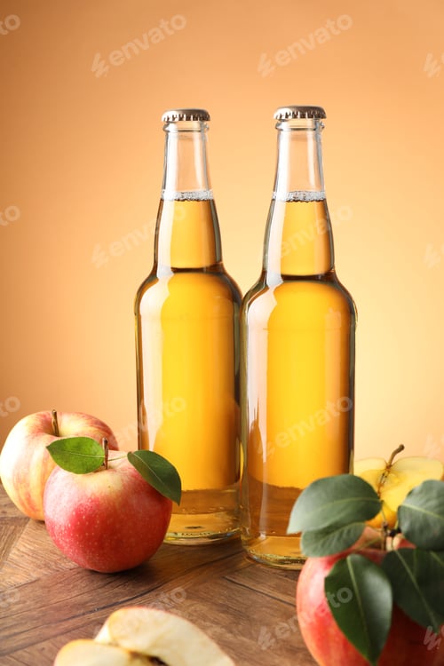 Preview: Delicious cider in glass bottles and apples on wooden table against orange gradient background