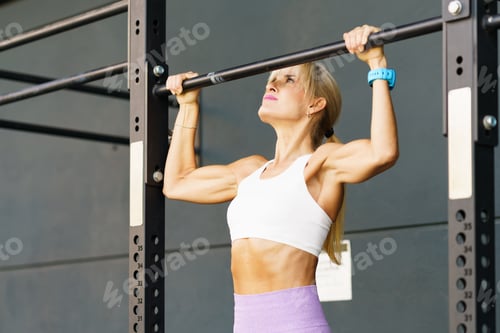 Preview: Strong young woman hanging on bar in gym