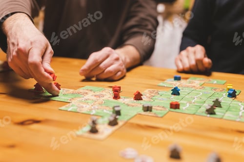 Preview: men friends have fun playing the carcassonne board game at night. male hands and game cards and chip