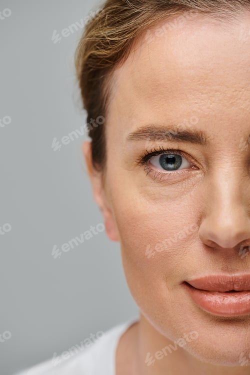 Preview: joyful good looking woman with contact lenses and blonde hair looking at camera on gray backdrop