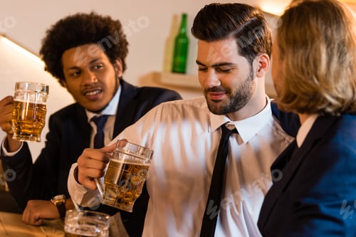 Preview: smiling young multiethnic businessmen drinking beer together in bar