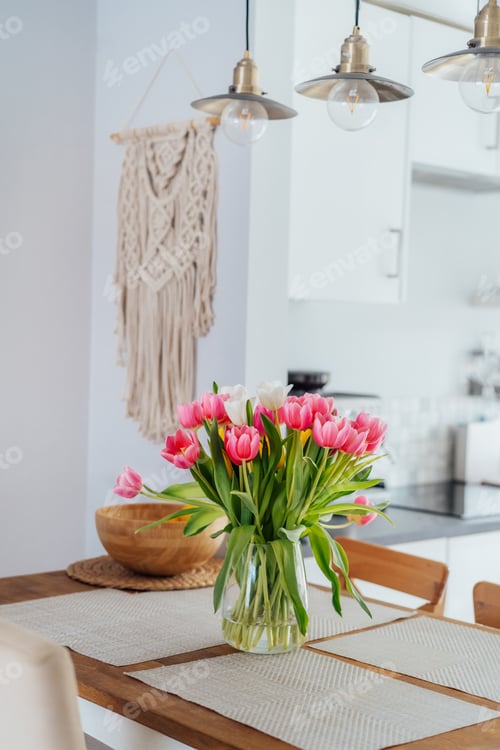 Preview: Stylish scandi interior of open space white kitchen with pink tulip flowers in vase on kitchen table