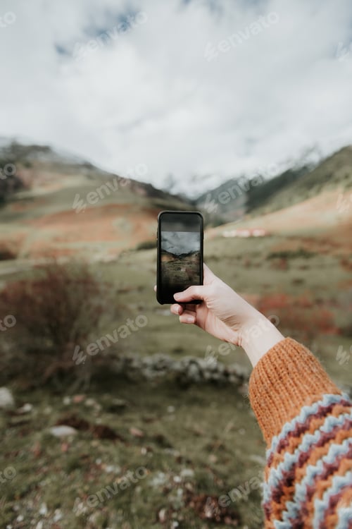Preview: Woman taking photo on smartphone of valley with high hills in cloudy weather