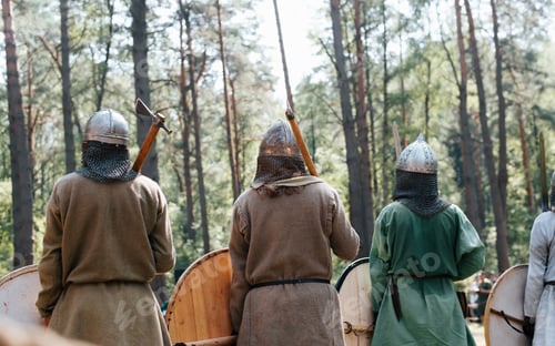 Preview: Vikings in medieval helmets with axes standing in the forest before the battle, back view