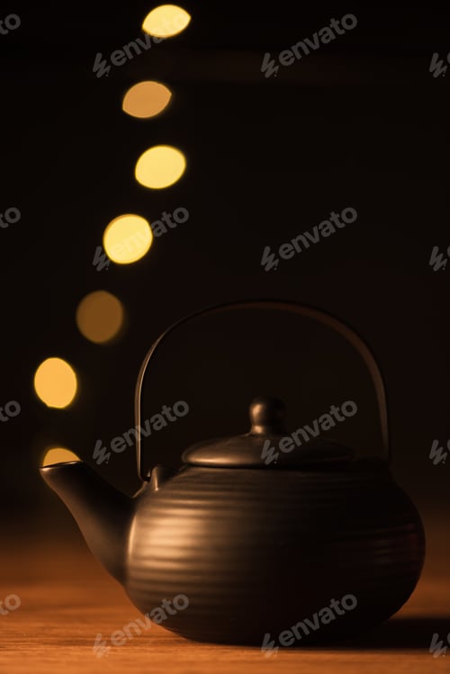 Preview: close up view of clay teapot and golden bokeh lights as steam on black background