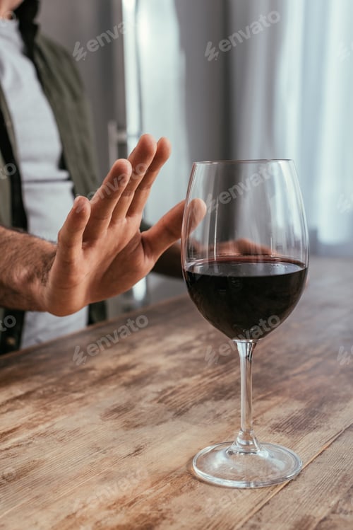 Preview: Cropped view of alcohol addicted man pulling hand to wine glass