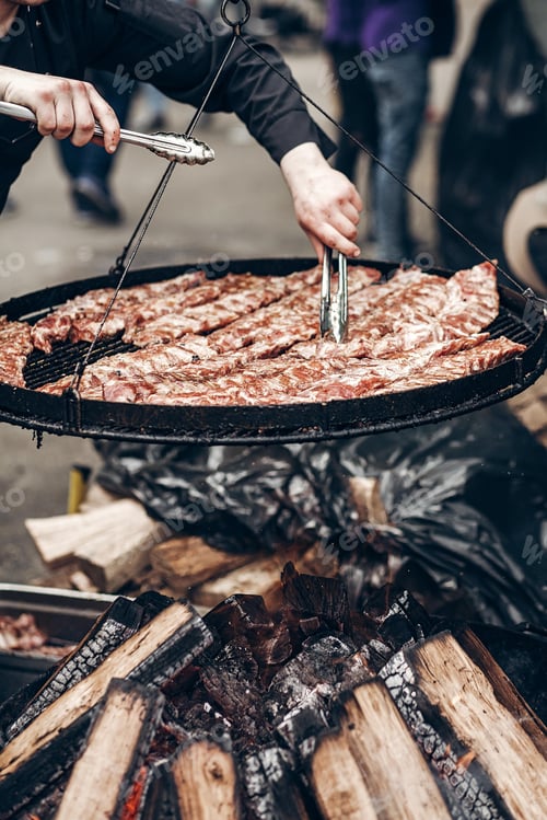 Preview: Grilled ribs meat. man holding steel tongues and roasting beef pork on big grill