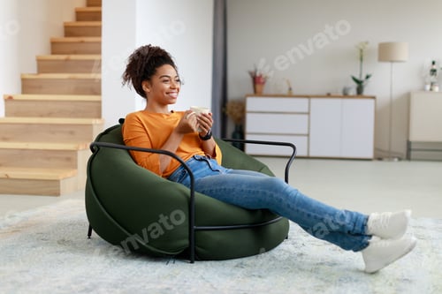 Preview: Calm black woman having rest at home drinking coffee