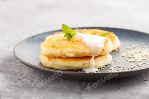 Preview: Cheese pancakes on a blue ceramic plate with milk sauce on a gray concrete background.