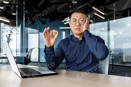 Preview: Dissatisfied and confused in depression asian financier investor, holding coin money crypto currency