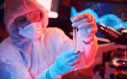 Preview: Nurse in mask and white uniform, holding tube with liquid and sitting in neon lighted laboratory