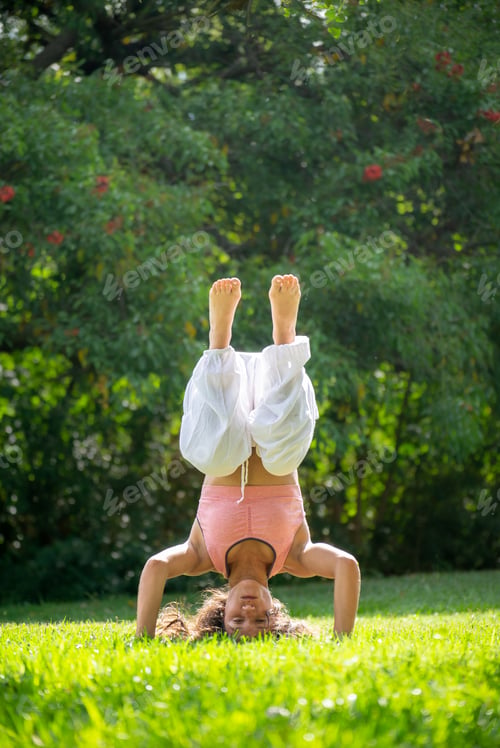 Preview: Young Woman Standing on her Heads Doing Yoga in a Green Park.Vertical Image