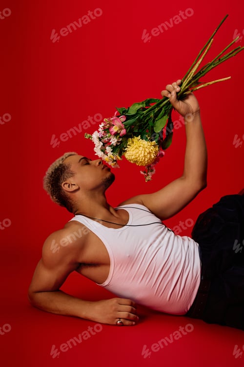 Preview: Young man showcases bold style with flowers in a vibrant red studio setting