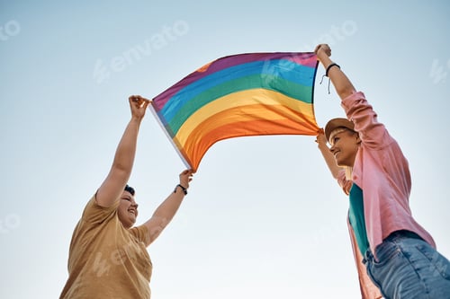 Preview: Below view of happy lesbian couple holding rainbow flag against the sky.