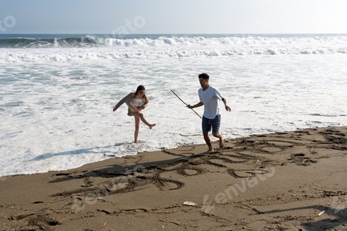 Preview: Young couple drawing in sand enjoying beach vacation
