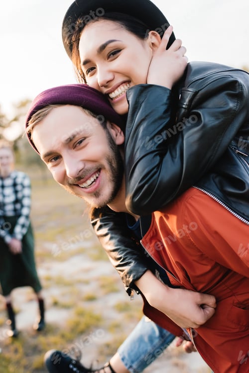 Preview: selective focus of happy coupe looking at camera while piggybacking together