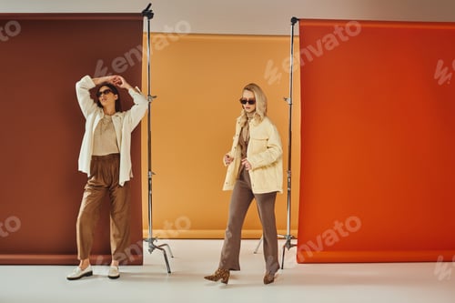 Preview: diverse cultures models in autumn outerwear and sunglasses posing on colorful backdrop, fall fashion