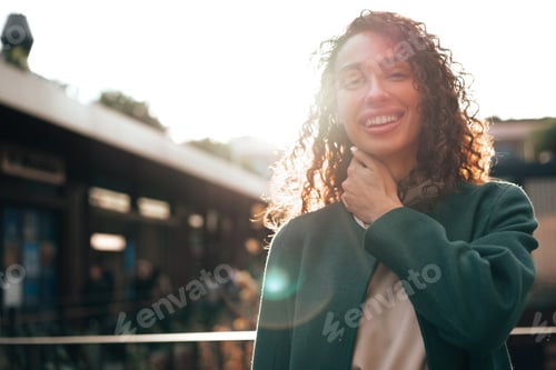 Preview: Portrait of young woman in green coat with curly hair in the city