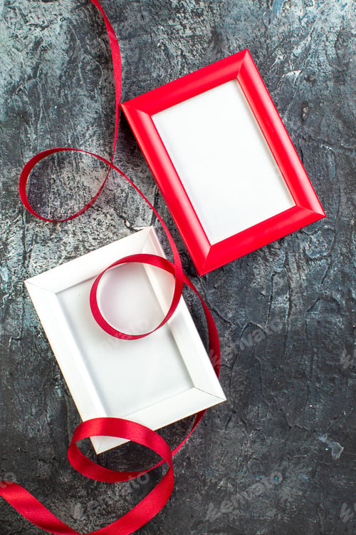 Preview: Vertical view of empty picture frames and ribbon on dark background