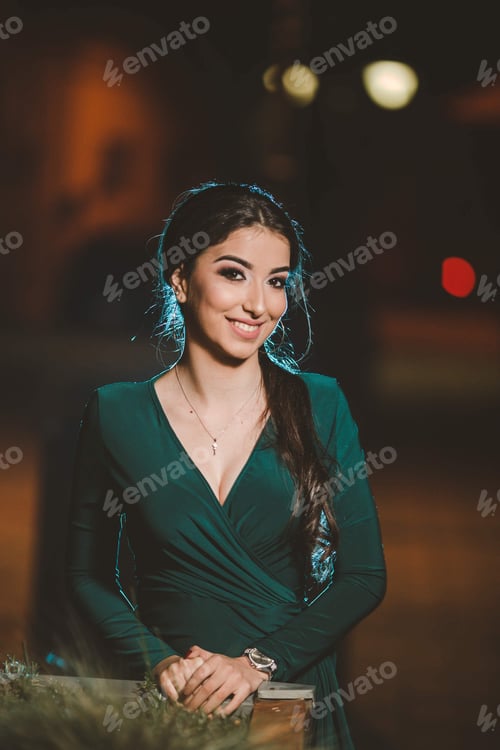 Preview: Vertical shot of a young Caucasian female posing in an elegant green dress in the street at night