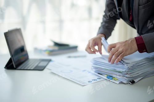 Preview: A man is sitting at a desk with a pile of papers in front of him