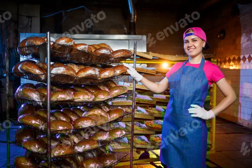 Preview: A young girl works in a bakery. She puts bread on a shelf. Woman baker at workplace in a bakery