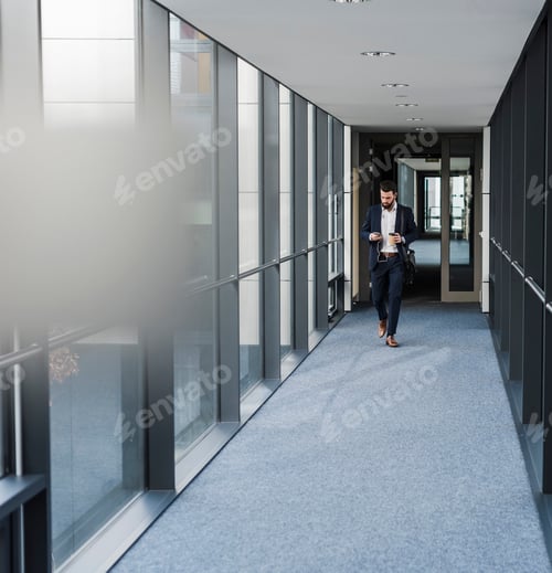 Preview: Businessman with earphones talking on smart phone in office building