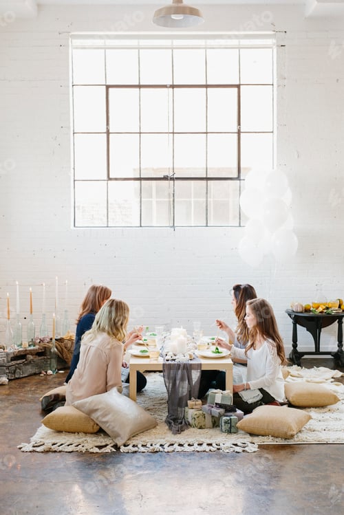 Preview: Four women seated at a low table on cushions.