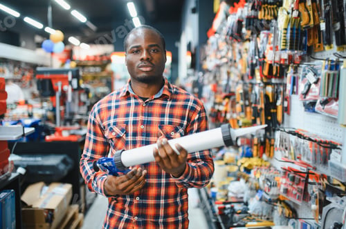 Preview: African american male customer in a modern hardware store chooses a silicone gun