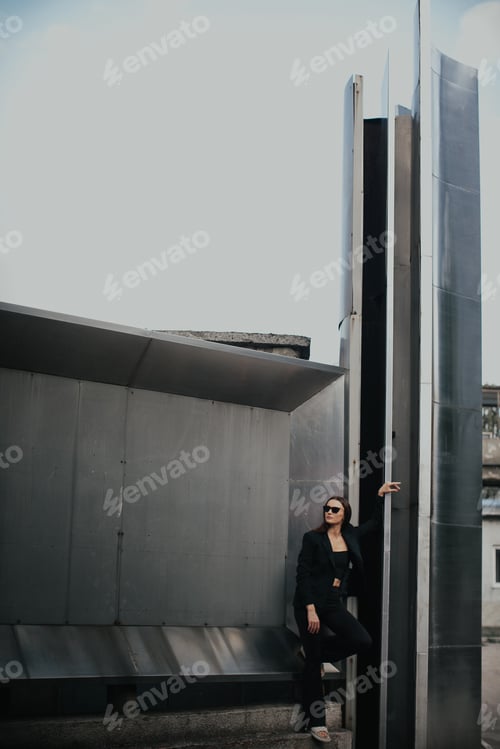 Preview: Fashion portrait of young elegant woman outdoors. Black suit, sunglasses, gray metal background.