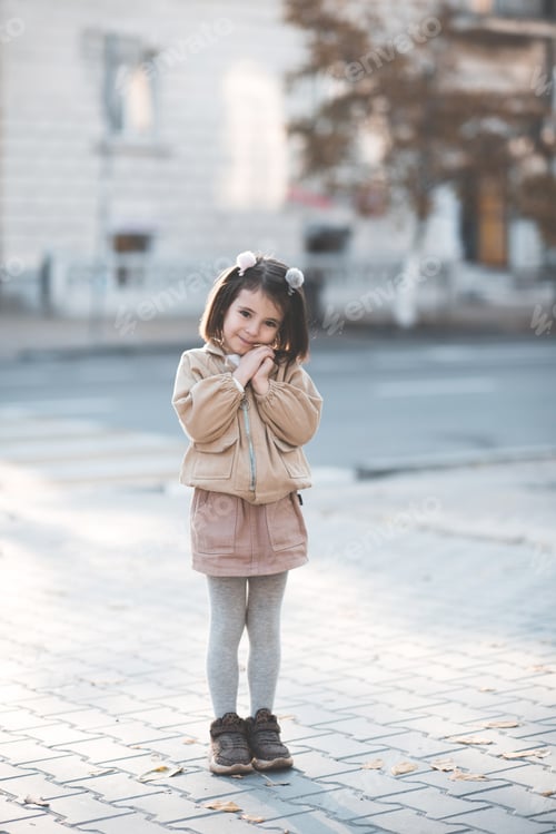 Preview: Cute kid girl 3-4 year old wearing trendy clothes posing in city outdoors.